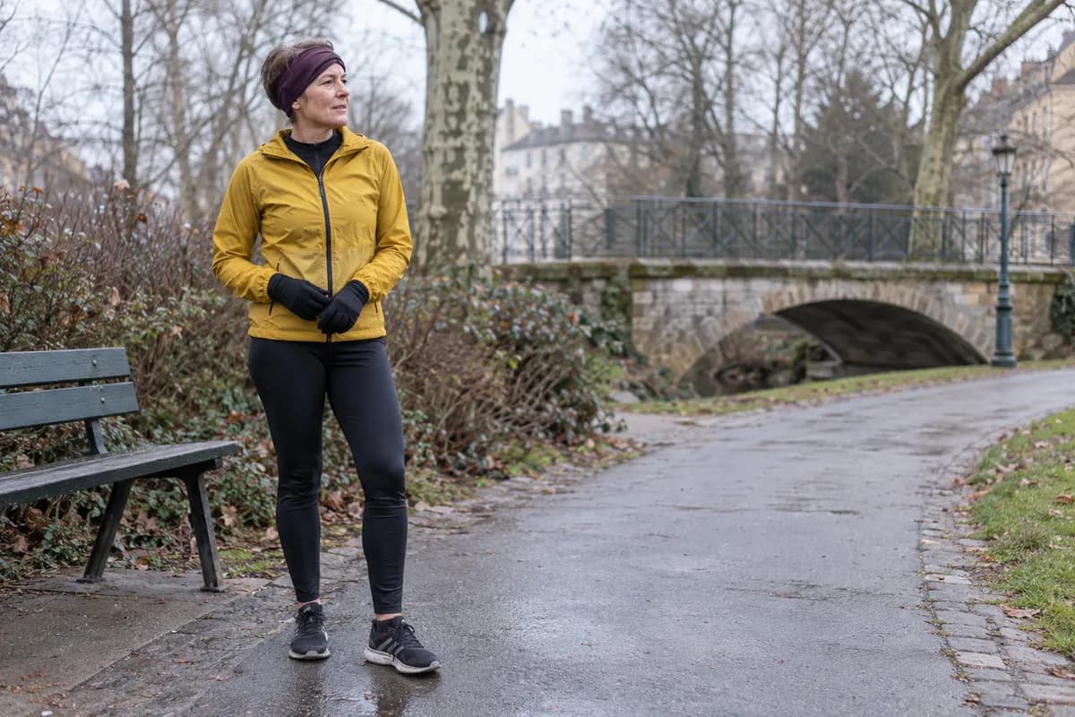 Hardloopster met windjack, tights, handschoenen en hoofdband tijdens een pauze in het park