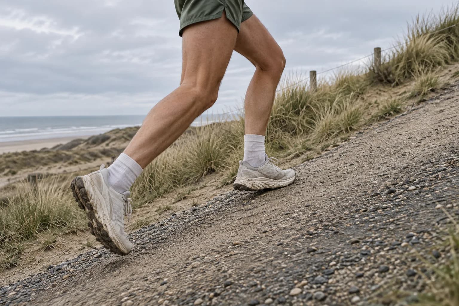 Close-up of a runner's legs running uphill on a firm dune path