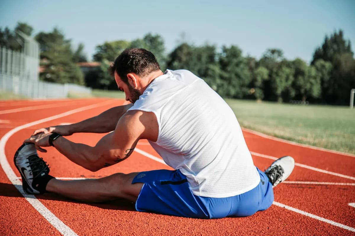Hardloper zit op een atletiekbaan en reikt naar de voet van zijn gestrekte been